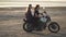 Beautiful young woman motorcyclist with his girlfriend riding a motorcycle in a desert on sunset or sunrise. Two woman on a bike.