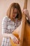 Beautiful young woman musician sitting on a vintage double bass on a beige background