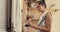 Beautiful young woman painting wooden door with paintbrush in terrace on summer