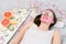 Beautiful young woman with pink alginate facial mask on her face and slices of fresh cucumber on her lying on the bed in