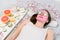 Beautiful young woman with pink alginate facial mask on her face and slices of fresh cucumber on her lying on the bed in