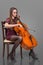 Beautiful young woman playing cello. Isolated on grey background