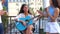 Beautiful young woman playing guitar sitting on a roof while youth having fun at a party. Positive female musician plays