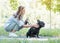 Beautiful young woman playing with her French bulldog in a park outdoors. General plan of pleased dog with short black