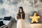 Beautiful young woman posing in bedroom on gray wall background and bright luminous decorative star