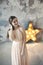 Beautiful young woman posing on gray wall and bright luminous decorative star