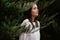 Beautiful young woman posing for a photographer in the park leaning against the branches of plants