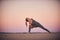 Beautiful young woman practices twist yoga asana Parivritta Parshvakonasana in the desert at sunset