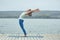 Beautiful young woman practices yoga asana Ardha Chakrasana - Half Wheel pose on the wooden deck near the lake