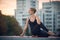 Beautiful young woman practices yoga asana Ardha Matsyendrasana - Half Spinal Twist pose outdoors against the background of a mode