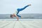 Beautiful young woman practices yoga asana Eka Pada Bakasana - one leg crane pose on the wooden deck near the lake