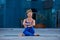 Beautiful young woman practices yoga asana Gomukhasana - Cow Face pose outdoors against the background of a modern city