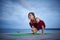 Beautiful young woman practices yoga asana Malasana - Garland pose on the wooden deck near the lake