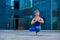 Beautiful young woman practices yoga asana Padangustha Padma Utkatasana - Half Lotus Toe Balance pose outdoors against the