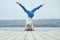 Beautiful young woman practices yoga asana Parshva Salamba Shirshasana - Headstand pose on the wooden deck near the lake