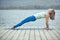 Beautiful young woman practices yoga asana Purvottanasana Upward Plank Pose on the wooden deck near the lake