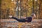 Beautiful young woman practices yoga asana Salabhasana locust pose on the wooden deck in the autumn park