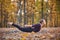 Beautiful young woman practices yoga asana Salabhasana locust pose on the wooden deck in the autumn park