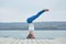 Beautiful young woman practices yoga asana Shirshasana - Headstand pose on the wooden deck near the lake