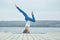 Beautiful young woman practices yoga asana Shirshasana - Headstand pose on the wooden deck near the lake