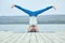 Beautiful young woman practices yoga asana Shirshasana - Headstand pose on the wooden deck near the lake