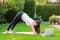 Beautiful young woman practicing yoga in garden outdoors following guide of online tutorial or trainer on laptop