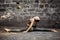 Beautiful young woman practicing yoga hanumanasana by a brick wall. Yoga concept.