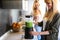 Beautiful young woman preparing detox juice in the blender and talking with friend at home.