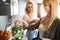 Beautiful young woman preparing detox juice in the blender and talking with friend at home.