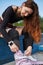 Beautiful young woman putting on inline skates in a skatepark. Cheerful white female with red hair sitting on a ledge in a skate
