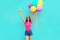 Beautiful young woman raising her hands up with bunch of balloons having fun wearing a shorts and pink t-shirt on blue wall