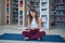 Beautiful young woman reading book and practices yoga asana Sukhasana - The Easy Sitting crosslegged Pose in the library