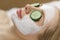 Beautiful young woman receiving facial mask of cucumber in beauty salon