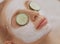 Beautiful young woman receiving facial mask of cucumber in beauty salon