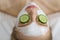 Beautiful young woman receiving facial mask of cucumber in beauty salon