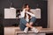 Beautiful young woman with red hair in jeans in a white shirt in sneakers sits on a wooden table in the kitchen with a stylish