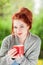 Beautiful young woman with red hair sitting in the garden, relaxing, drinking coffee