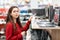 Beautiful young woman in a red sweater, choosing a laptop. In the background, shelves with electronics. Close up. Concept of