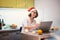 Beautiful young woman in santa hat celebrates christmas and new year at home using laptop internet, cheers with a glass of