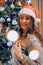 Beautiful young woman in santas hat decorating christmas tree. New year decoration. Home interior. Winter holidays