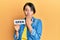 Beautiful young woman with short hair holding banner with open text covering mouth with hand, shocked and afraid for mistake