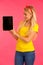 Beautiful young woman sin yellow t shirt holds tablet and surfs internet over pink background