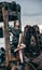 Beautiful young woman sits on a metal rusty detail, an abandoned factory