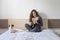 beautiful young woman sitting on bed with her cute small dog besides. Home, indoors and lifestyle. She is drinking orange juice.
