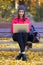 Beautiful young woman sitting in a bench and using her laptop in autumn.