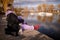 Beautiful young woman sitting on the edge of wooden jetty by the lake with autumn reflections