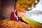 Beautiful young woman sitting in fallen leaves at autumn park