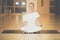 Beautiful young woman sitting in Lotos pose and practicing meditation in yoga hall