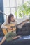 Beautiful young woman sitting on sofa playing guitar