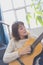 Beautiful young woman sitting on sofa playing guitar